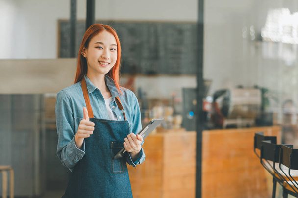 Lächelnder asiatischer Coffeeshop-Besitzer, der mit Tablet vor der Kasse steht, um Menübestellungen entgegenzunehmen. Willkommen bei Kunden, die kommen, um im Café zu bestellen. - Foto, Bild