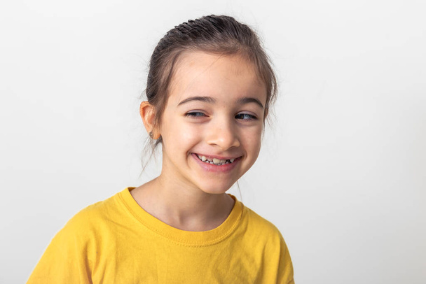 Funny little Caucasian girl in a yellow T-shirt smiles slyly on a white background isolated, the sly look of a child, copy space. - Photo, Image