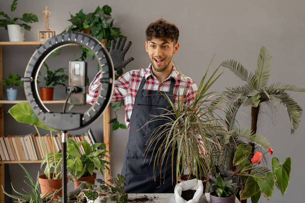 Young man influencer blogger blogging about houseplants, filming on a smartphone on a tripod. Copy space - Foto, immagini