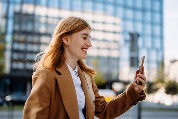Uśmiechnięty lider biznesu patrząc na telefon komórkowy podczas spaceru w centrum biznesowym. Wysokiej jakości zdjęcie - Zdjęcie, obraz