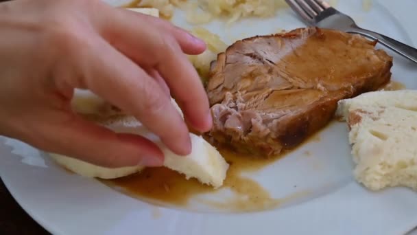Prága, Csehország, 2023. augusztus 4. Közelkép lassított felvételben az egyik tipikus ételekkel: párolt sertés savanyú káposztával és kenyérrel a mártáshoz. A kéz megragadja a kenyeret és belemártja a húsos szószba.. - Felvétel, videó