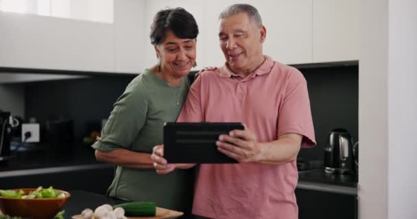 Tablet, video call and senior couple in kitchen for lunch or supper meal at modern home. Happy, food and elderly man and woman on virtual conversation with digital technology cooking dinner - Footage, Video