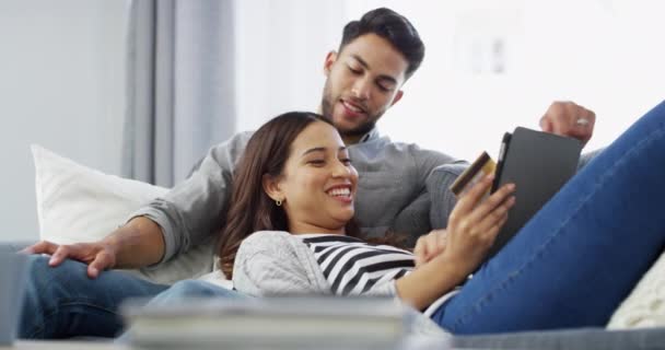Couple, tablet and credit card for online shopping with laughing, conversation and happiness with lying on sofa. Man, woman and internet payment with technology, relaxing and smile on couch of lounge. - Footage, Video