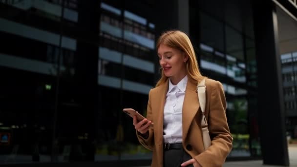 Iloinen nainen johtaja kävely kaupunki tilalla moderni älypuhelin pilvinen päivä. Houkutteleva liikenainen lukemassa matkaviestejä liikkeellä. Happy Lady ceo yllään tyylikäs valkoinen paita näköinen puhelin näyttö  - Materiaali, video