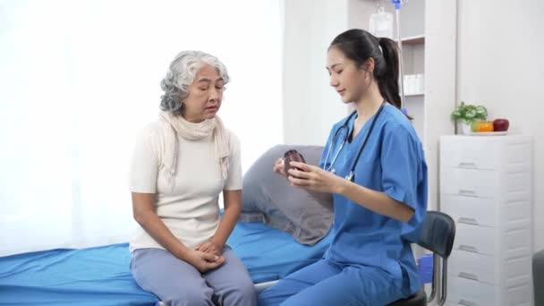Медсестра из Азии проверяет пожилую азиатку на больничной койке. Привлекательный сиделка поддерживает, дает советы и консультации с пожилой бабушкой в clinic.4k 60p - Кадры, видео