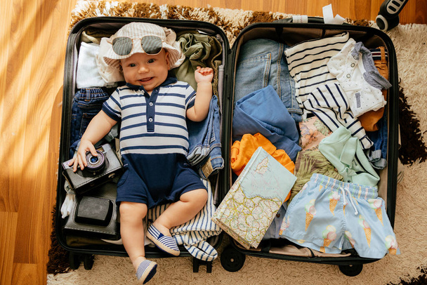 Bebé en maleta de viaje. Niño dentro de equipaje embalado para vacaciones lleno de ropa, viaje de niño y familia
 - Foto, imagen