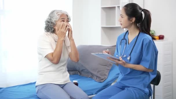 Aziatische verpleegkundige controleert senior Aziatische vrouwelijke patiënt op ziekenhuisbed. Aantrekkelijke verzorger ondersteunt, adviseert en adviseert oudere grootmoeder in kliniek.4k 60p - Video