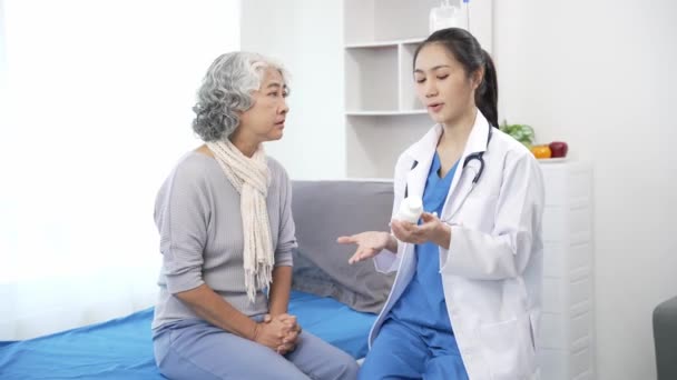 Aziatische verpleegkundige controleert senior Aziatische vrouwelijke patiënt op ziekenhuisbed. Aantrekkelijke verzorger ondersteunt, adviseert en adviseert oudere grootmoeder in kliniek.4k 60p - Video