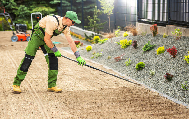Jardinero caucásico en sus años 40 Preparando el suelo del patio trasero residencial para una siembra de hierba. Rastrillar el suelo. - Foto, Imagen
