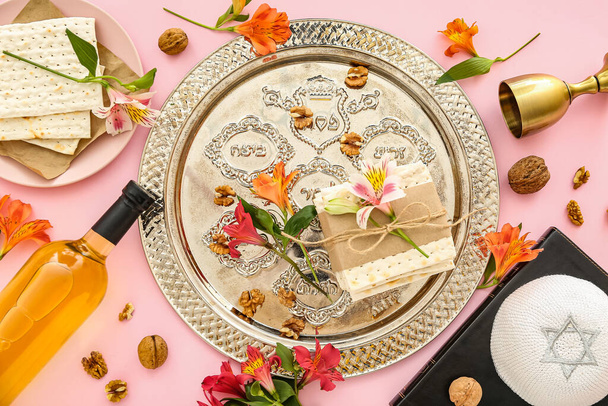 Composition with Passover Seder plate, flatbread matza, bottle of wine, Torah and flowers on pink background - Foto, Bild