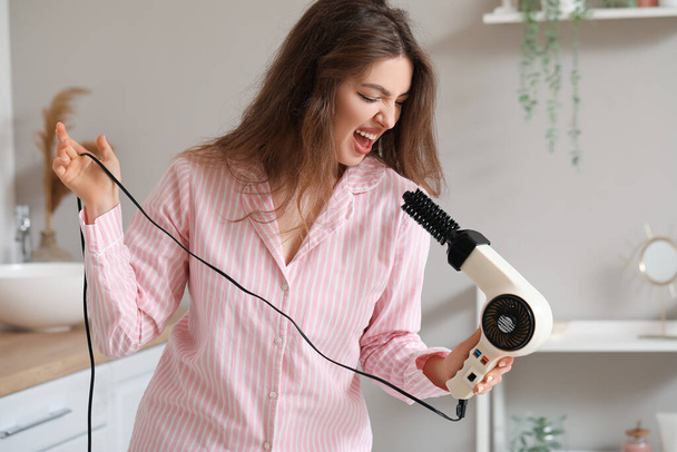 Pretty young woman with hair dryer singing in bathroom - Photo, Image