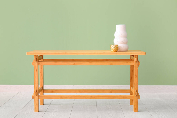 Dřevěný stůl s vázou a šálkem u zelené stěny - Fotografie, Obrázek