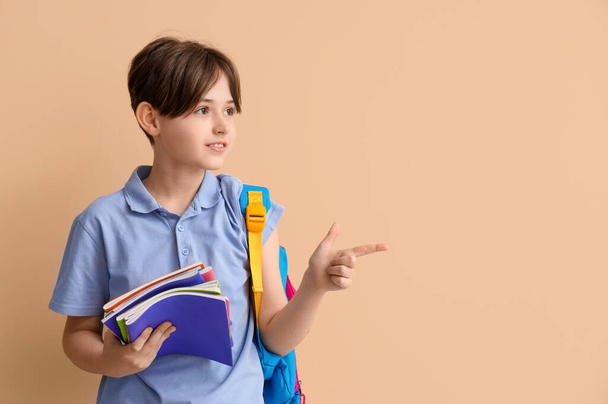 Malý školáček s copybooks ukazující na něco na béžovém pozadí - Fotografie, Obrázek