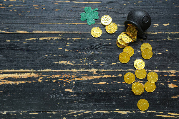 Pot with golden coins and paper clover on black wooden background. St. Patrick's Day celebration - Zdjęcie, obraz