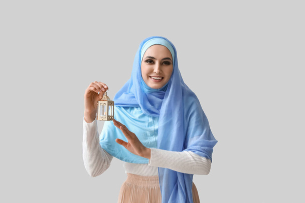 Mujer musulmana joven con linterna sobre fondo claro. Celebración del Año Nuevo Islámico - Foto, imagen
