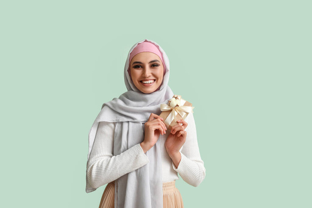 Young Muslim woman with gift on green background. Islamic New Year celebration - Foto, imagen