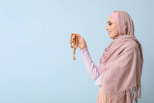 Young Muslim woman with prayer beads on blue background. Islamic New Year celebration - Фото, изображение