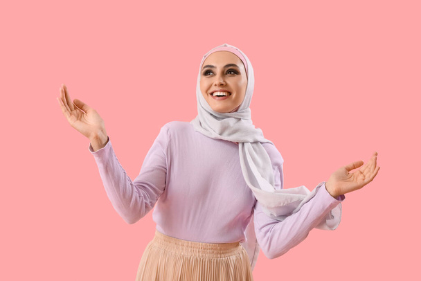 Young Muslim woman on pink background. Islamic New Year celebration - Foto, imagen