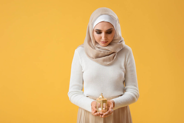 Young Muslim woman with lantern on yellow background. Islamic New Year celebration - Zdjęcie, obraz