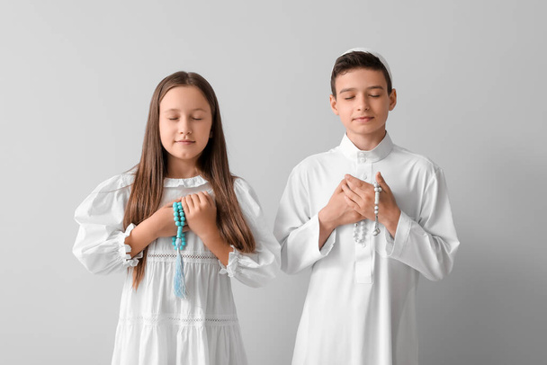 Little Muslim children with praying beads on light background - Foto, Imagen