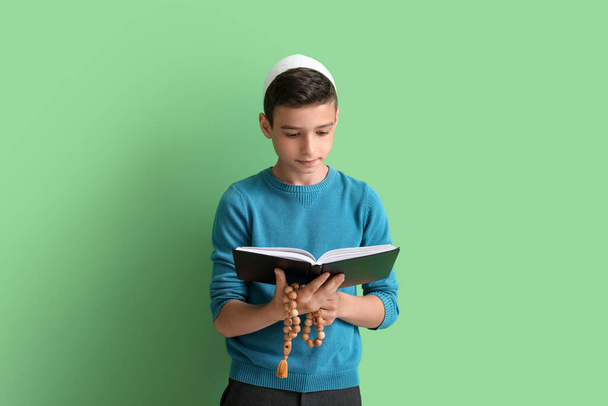 Little Muslim boy with Quran and praying beads on green background - Foto, Imagen