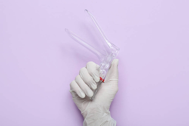 Mano en guante médico y con espéculo ginecológico sobre fondo lila - Foto, imagen