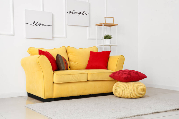 Żółta sofa z poduszkami i puf w pobliżu białej ściany - Zdjęcie, obraz