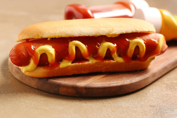 Wooden board with tasty hot dog on brown background - Фото, зображення