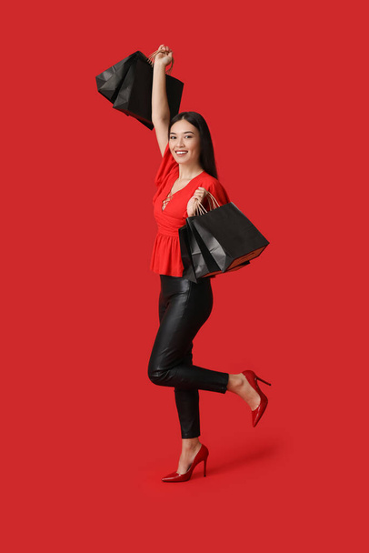 赤い背景のショッピングバッグを持つ美しい若いアジアの女性. ブラックフライデーセール - 写真・画像