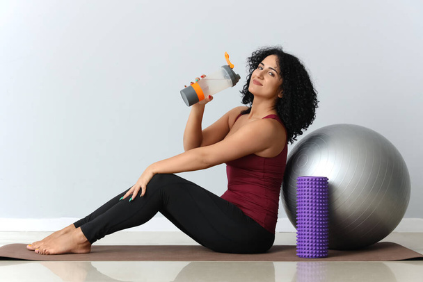 Sporty adult woman with fitball drinking water on grey background - Photo, Image