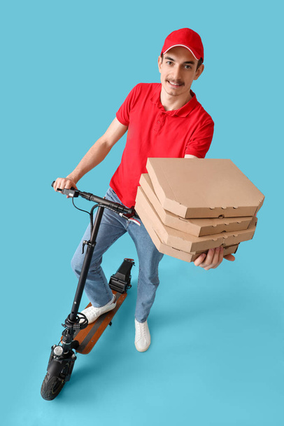 Male courier with pizza boxes and kick scooter on blue background - 写真・画像