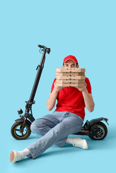 Male courier with pizza boxes and kick scooter on blue background - Zdjęcie, obraz