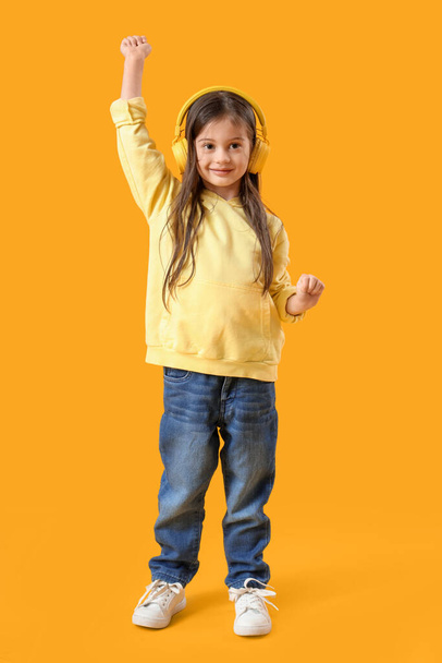 Cute little girl in headphones dancing on yellow background - Fotografie, Obrázek