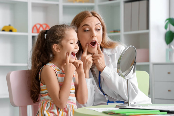 Mature speech therapist working with little girl near mirror at table in office - Фото, зображення