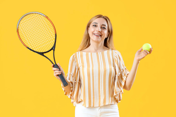 Mature woman with tennis racket and ball on yellow background - Photo, image