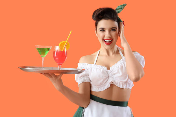 Young pin-up waitress with cocktails on orange background - Photo, Image