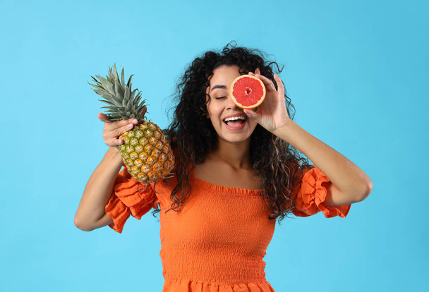 Young African-American woman with pineapple and grapefruit on blue background - Фото, зображення