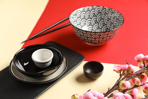 Schalen mit Tassen, Essstäbchen und Sakura-Ast auf farbigem Hintergrund. Chinesische Tischdekoration - Foto, Bild