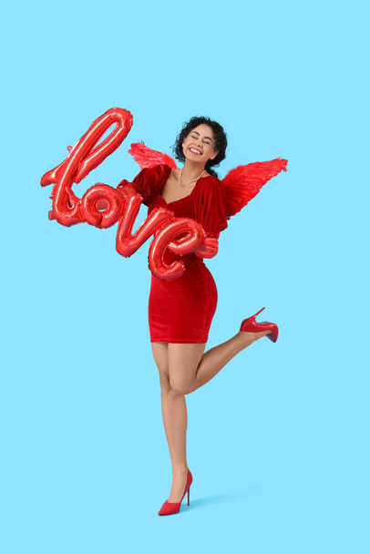 Young African-American woman dressed as Cupid with word LOVE made of balloons on blue background. Valentine's Day celebration - Фото, изображение