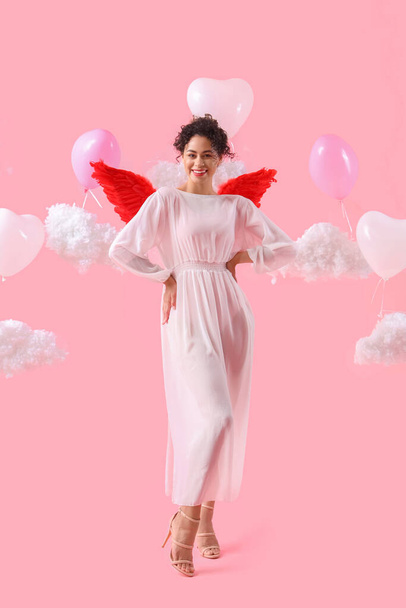 Young African-American woman dressed as Cupid with balloons and clouds on pink background. Valentine's Day celebration - Foto, immagini