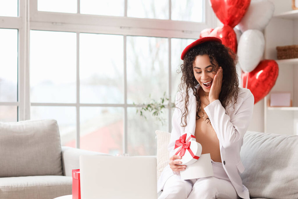 Surprised young African-American woman opening gift box at home on Valentine's Day - Foto, Bild