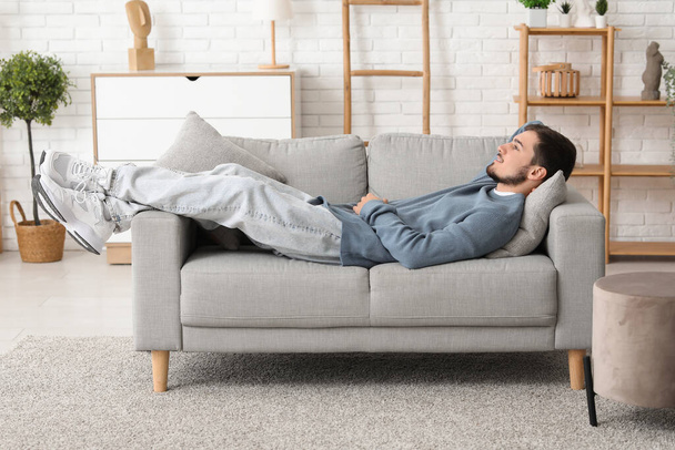 Handsome young man lying on sofa in living room - Photo, image