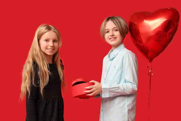 Little boy greeting girl with gift on red background. Valentine's Day celebration - Fotó, kép