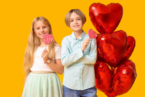 Little children with lollipops and heart-shaped balloons on yellow background. Valentine's Day celebration - Foto, Bild