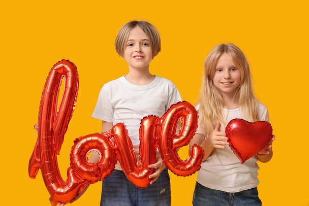Little children with word LOVE and balloon on yellow background. Valentine's Day celebration - Фото, зображення