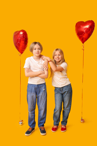 Little children with heart-shaped balloons on yellow background. Valentine's Day celebration - Фото, изображение