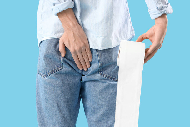 Young man with hemorrhoids and toilet paper on blue background, back view - 写真・画像