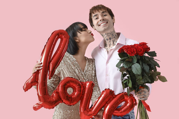 Young couple with word LOVE and roses on pink background. Valentine's Day celebration - Foto, Bild
