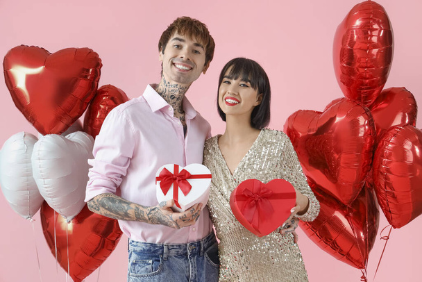 Young couple with gift boxes and balloons on pink background. Valentine's Day celebration - Foto, Imagen