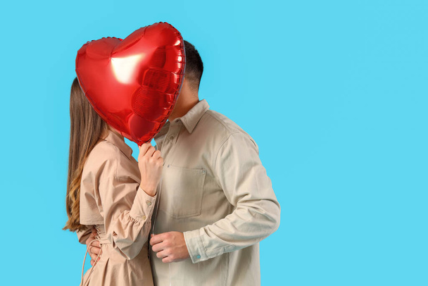 Lovely couple covering face with heart-shaped balloon on blue background. Valentine's Day celebration - Φωτογραφία, εικόνα